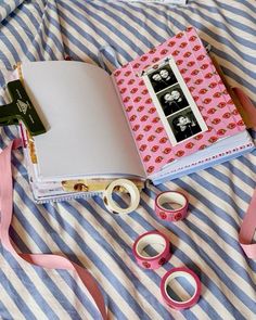 an open book sitting on top of a bed next to some pink tape and scissors