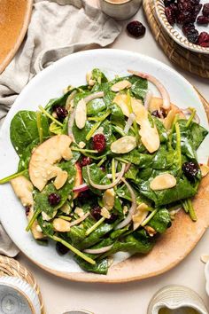 spinach salad with apples, cranberries and almonds on a white plate