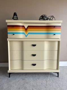 an old dresser painted with multicolored stripes and black knobs on the top