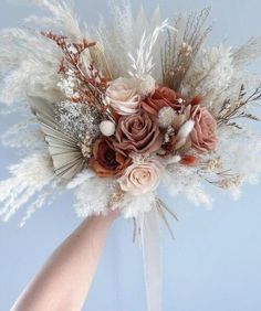 a bridal bouquet with dried flowers and feathers in the palm of someone's hand