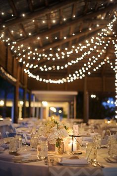 the tables are set with white linens and lit up by fairy lights in the ceiling