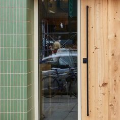 the reflection of a woman in a window with a bicycle parked outside it and another person walking by