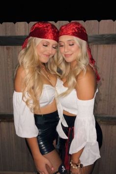 two beautiful young women standing next to each other in front of a wooden wall wearing red bandanas