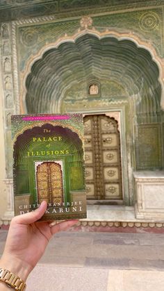 a person holding up a book in front of an ornate building with arches and doorways