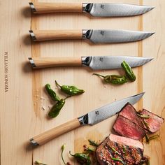 four steaks on a cutting board with knives and peppers