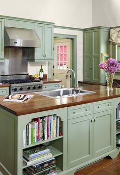 a kitchen with green cabinets and an island in front of the sink, bookshelves