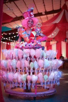 a woman dressed in pink and white is standing on top of a cake with lollipops