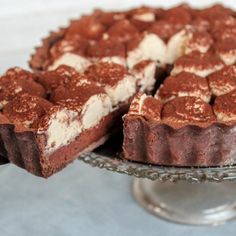 a chocolate pie with white frosting on a glass cake plate next to a slice missing from it