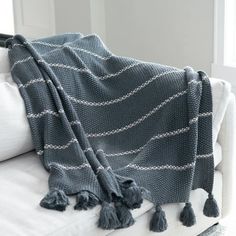 a gray and white blanket sitting on top of a couch next to a pillow with tassels