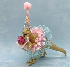 a toy dinosaur wearing a pink and blue dress with a birthday hat on it's head