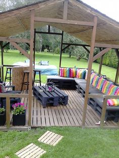 a wooden deck with couches and tables under a roof over looking a grassy area