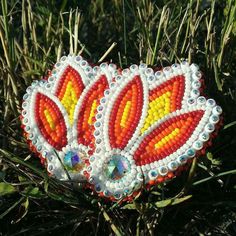 an orange and yellow beaded brooch sitting in the grass