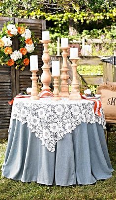 an outdoor table with candles and flowers on the table cloth is set up in front of a wooden fence