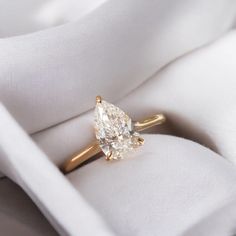 an engagement ring with a pear shaped diamond in it on top of a white cloth