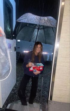 a woman standing under an umbrella in the rain holding a box with some candy on it