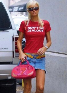 a woman in red shirt and denim shorts carrying a pink handbag