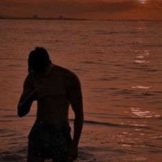 a man standing in the water at sunset with his cell phone up to his ear