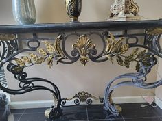 an ornate black and gold console table with two vases on the shelf above it