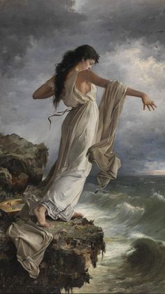 a woman standing on top of a rocky cliff next to the ocean with her arms outstretched