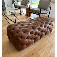 a brown leather couch sitting on top of a hard wood floor next to two chairs