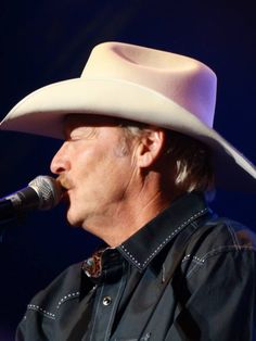 a man in a cowboy hat singing into a microphone with his hand on his hip