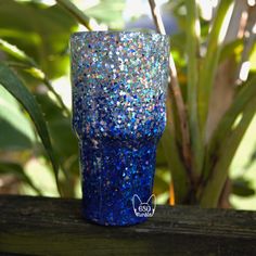 a blue glittered cup sitting on top of a wooden table next to a plant