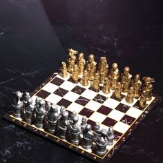 a chess board with gold and silver pieces on it, sitting on a marble surface