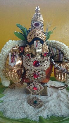 a statue of the god ganesh in gold and red with white flowers around it