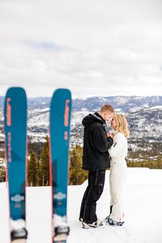 Engaged couple stands in ski attire holding hands. Background snowy mountains, foreground blue skis. Ski Proposal Engagement, Ski Engagement Photos, Vail Photoshoot, Ski Proposal, Ski Engagement, Skiing Couple, Ski Photos