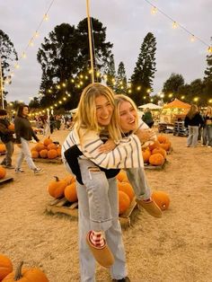 two women hugging each other in front of pumpkins