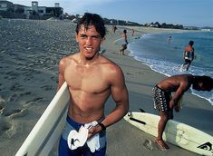 a man holding a surfboard on top of a sandy beach next to the ocean