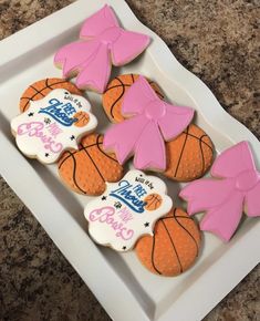 decorated cookies in the shape of basketballs and bows on a white plate with granite counter top