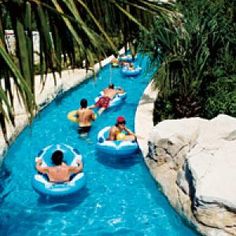 several people are tubling down the water in an artificial swimming pool that is surrounded by rocks and palm trees