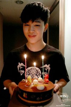 a young man holding a cake with lit candles