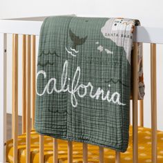 a baby crib with a green blanket hanging from it's side and the word california written in white