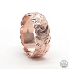 a rose gold wedding ring with flowers on the side and leaves in the middle, set against a white background