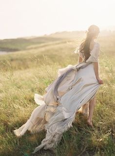 a woman in a white dress is walking through the grass