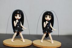 two small figurines with black hair on wooden bases