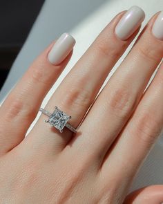 a woman's hand with white nails and a ring on her finger, holding an engagement ring