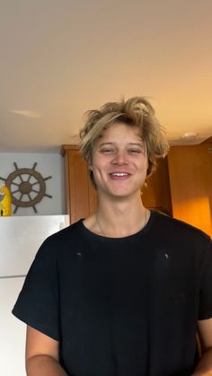 a young man standing in front of a refrigerator with his arms crossed and smiling at the camera