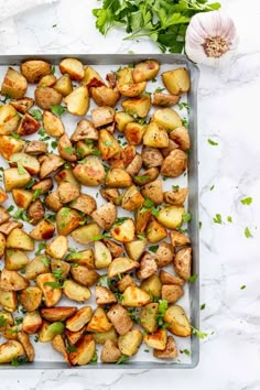 roasted potatoes on a baking sheet with parsley and garlic next to it, ready to be cooked