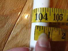 a person holding a measuring tape next to a white tube on a wooden table with wood flooring