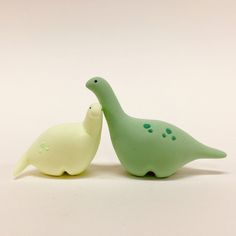 two small plastic toy dinosaurs sitting next to each other on a white surface, one is green and the other is yellow