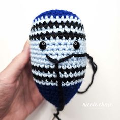 a hand holding a crocheted blue and black striped ball with eyes on it