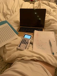 an open laptop computer sitting on top of a bed next to a calculator