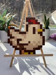 a pixelated chicken sitting on top of a wooden easel next to a potted plant