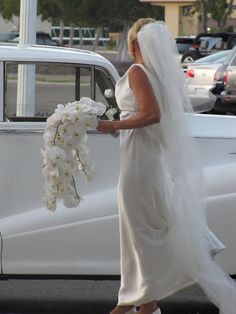 a woman in a white dress is walking by a car with flowers on the side