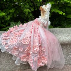 a stuffed animal in a pink dress sitting on a stone ledge next to some bushes