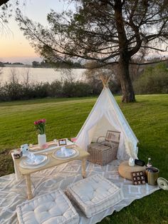 a table with plates and cups on it in the grass next to a teepee