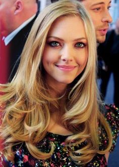 a woman with long blonde hair and blue eyes smiling at the camera while standing next to a man